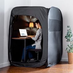 a person sitting at a desk with a laptop in a portable office tent on the floor