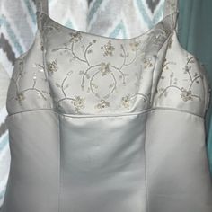 the back of a white dress with flowers and beads on it's shoulders, in front of a patterned curtain