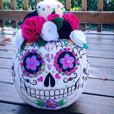 a decorated pumpkin sitting on top of a wooden deck with flowers in the skull shape