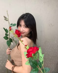 a woman is holding two roses in her hand and posing for the camera while wearing a brown dress