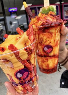 two people holding up drinks in front of a storefront window, one is filled with fruit and the other has strawberries on it