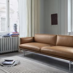 a tan leather couch sitting in front of a window next to a radiator