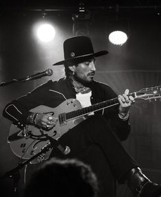 a man with a hat playing an electric guitar in front of microphones on stage