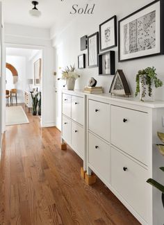 a hallway with white walls and wooden floors, framed pictures on the wall above it