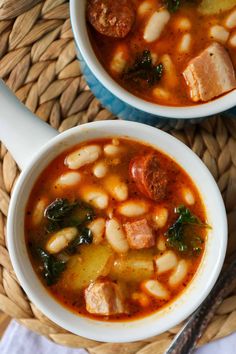 two bowls of soup with sausage, beans and spinach in it on a wicker place mat