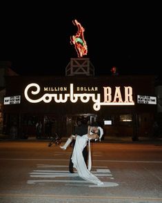 a man and woman dance in front of a neon sign that says cowboy bar