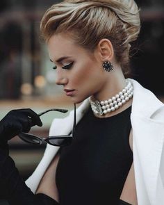 a woman wearing black gloves and pearls on her head, holding a pair of glasses