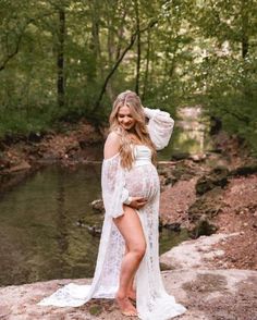 a pregnant woman poses in front of a river while wearing a white lace cover - up