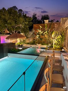 an outdoor swimming pool at night with chairs around it and trees in the background, surrounded by greenery