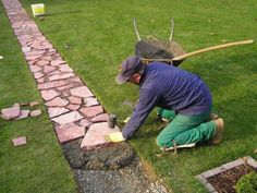 a man with a wheelbarrow is working on some bricks in the grass next to a brick path