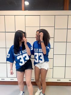 two girls in blue jerseys standing next to each other with their hands on their faces