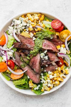 a white bowl filled with steak, corn and tomatoes on top of a table next to a fork