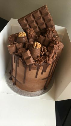 a cake with chocolate icing and nuts on top sitting in a white cardboard box