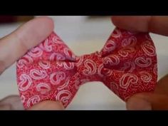 two hands holding a red bow tie with white paisley designs on it and one hand is tying the ribbon