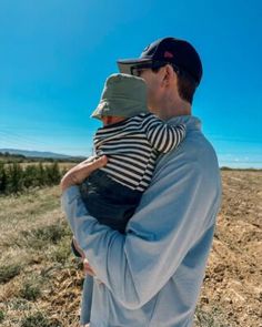 a man holding a baby in his arms while standing on top of a dry grass field