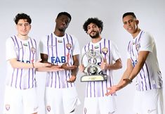 three men in soccer uniforms holding a trophy