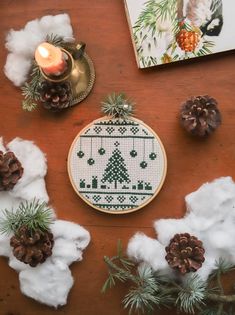 a cross stitch christmas ornament surrounded by pine cones and other holiday decor items