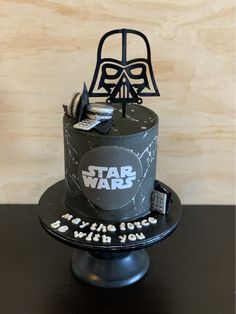 a star wars themed birthday cake on a black plate with silver letters and a darth vader mask