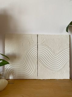 some plants are sitting on a table next to a white wall with wavy lines painted on it