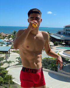 a man in red trunks drinking from a yellow cup