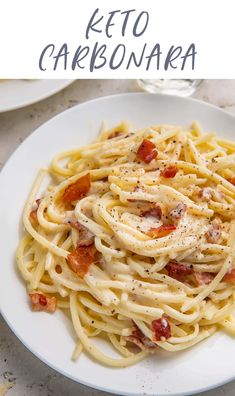 a white plate topped with pasta covered in sauce and bacon next to a glass of wine