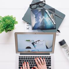 a woman's hands on the keyboard of her laptop computer, surrounded by office supplies