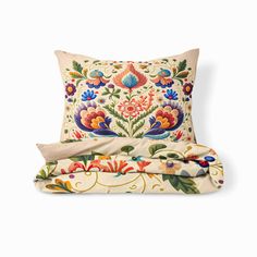 an embroidered pillow with colorful flowers and leaves on the front, along with two matching throw pillows