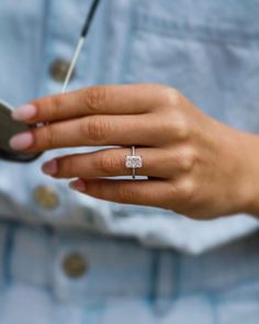 a woman's hand holding a cell phone with a diamond ring on her finger