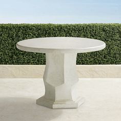 a white table sitting on top of a cement floor next to a green hedge covered wall