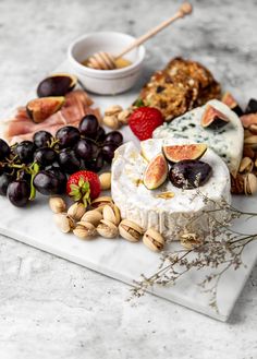 an assortment of cheeses, fruits and nuts on a marble platter