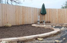 a backyard with an umbrella and some rocks in the ground next to a wooden fence