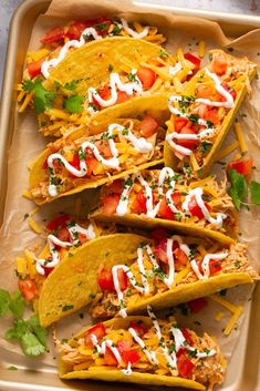 four tacos with shredded cheese, tomatoes and cilantro on a baking sheet