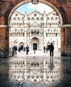 people are standing in front of a building with an arched doorway and reflection on the ground