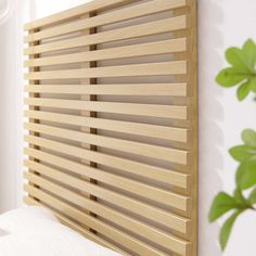 a bed with white sheets and wooden slatted headboard next to a plant