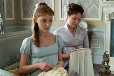 two women sitting on a couch in front of a mirror looking at an old book