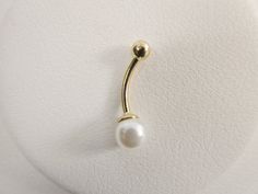 a gold nose ring with a single pearl on the end, mounted on a white surface