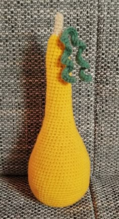 a crocheted yellow pear sitting on top of a gray couch next to a black and white pillow