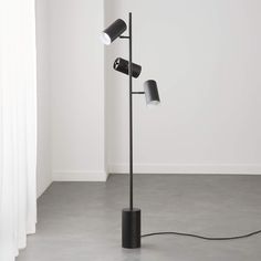 a black lamp with three lamps on it in a white room next to a window