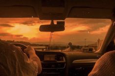 two people driving in the back seat of a car at sunset