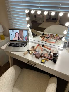 a laptop computer sitting on top of a white desk next to a mirror with lights