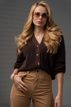 a woman with long blonde hair wearing brown pants and a cardigan sweater is posing for the camera