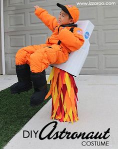 a young boy dressed in an orange and yellow costume sitting on top of a cardboard box