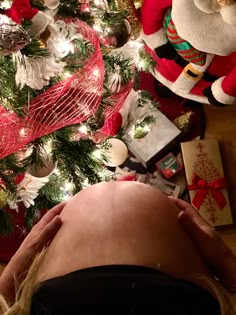 a pregnant woman laying in front of a christmas tree