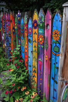 colorful painted wooden fence with flowers growing in the foreground and behind it is a garden