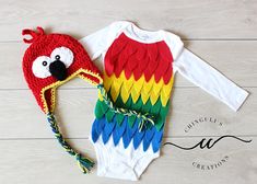 a red, yellow and green bird bodysuit with matching headband next to a crocheted hat