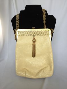 A stunning, vintage clutch/evening bag. This bag is made by Triangle New York, and was made in the 1940s. It is rectangle shape with rounded corners. The body of the bag is an ivory patent leather. It has a gold tone frame that has a wonderful, oval chain link design on the front. And the best part, is a gold tone ball and tassel that sways in the front. The lining is a navy corduroy with a gold lined inner pocket. This bag has a snap clasp and a gold chain strap, that can be worn long or double Cream Rectangular Shoulder Bag For Evening, Cream Rectangular Shoulder Bag For Evenings, Elegant Cream Rectangular Evening Bag, Cream Clutch Shoulder Bag For Evening, Cream Rectangular Evening Bag, Elegant Cream Rectangular Clutch, Retro Rectangular Evening Bag For Vintage Fashion, Retro Rectangular Evening Bag For Formal Occasions, Cream Clutch Evening Bag For Formal Occasions