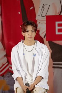 a man sitting on top of a wooden chair in front of a red and white wall