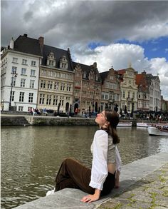 a woman sitting on the side of a river next to buildings