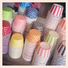 there are many different colored polka dot paper cups on the table with flowers in the background