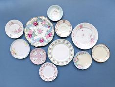 an assortment of china plates and saucers on a blue background, including one with pink flowers